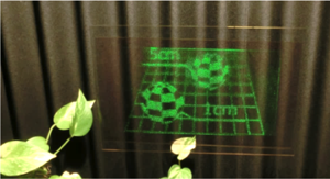 ホログラフィック3D映像技術。透明な板に緑色の図形や文字が表示されている。